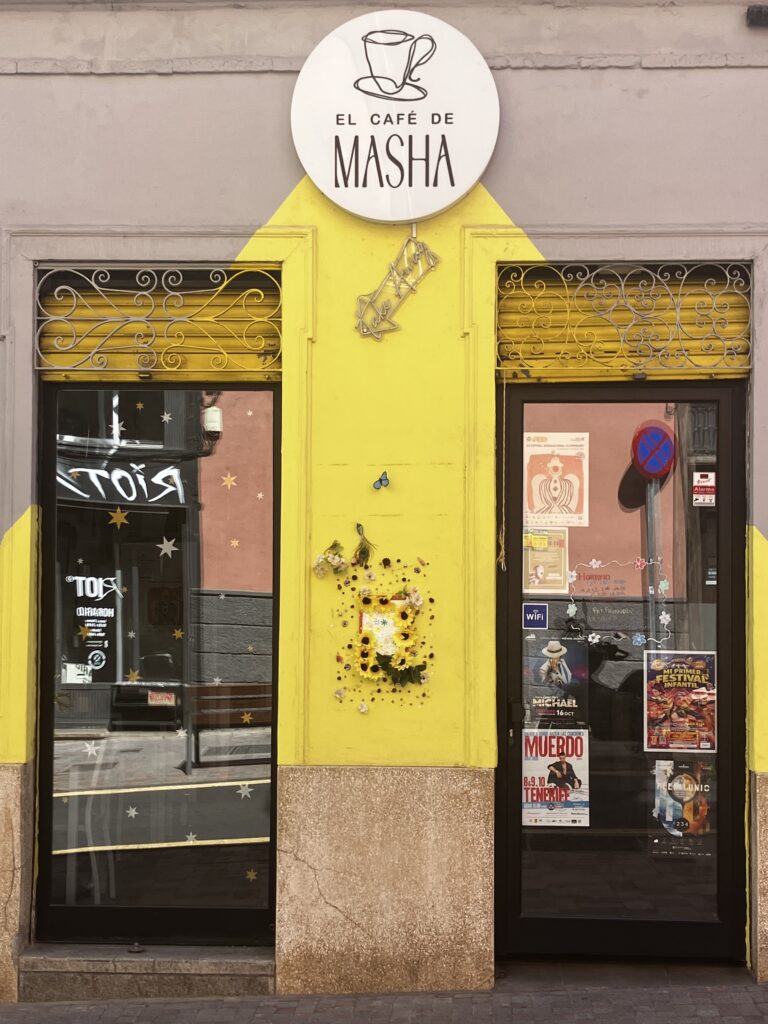 El Café de Masha Tenerife. A photo from the outside of the cafe looking at the sign and two large windows looking out to the street.