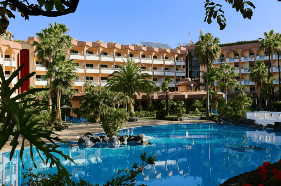 Puerto Palace Hotel in the background, pool and landscaped grounds with palm trees in front. Best family-friendly hotels in Puerto de la Cruz, Tenerife