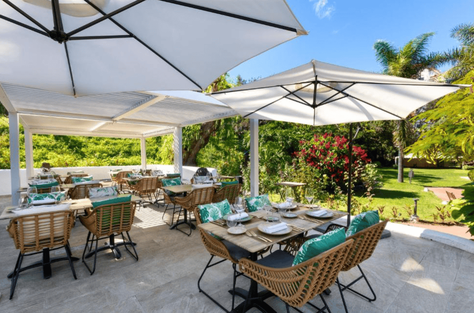Parque Vacaional Eden in Puerto de la Cruz, Tenerife. Multiple tables set up for outdoor dining, covered by sun umbrellas. 