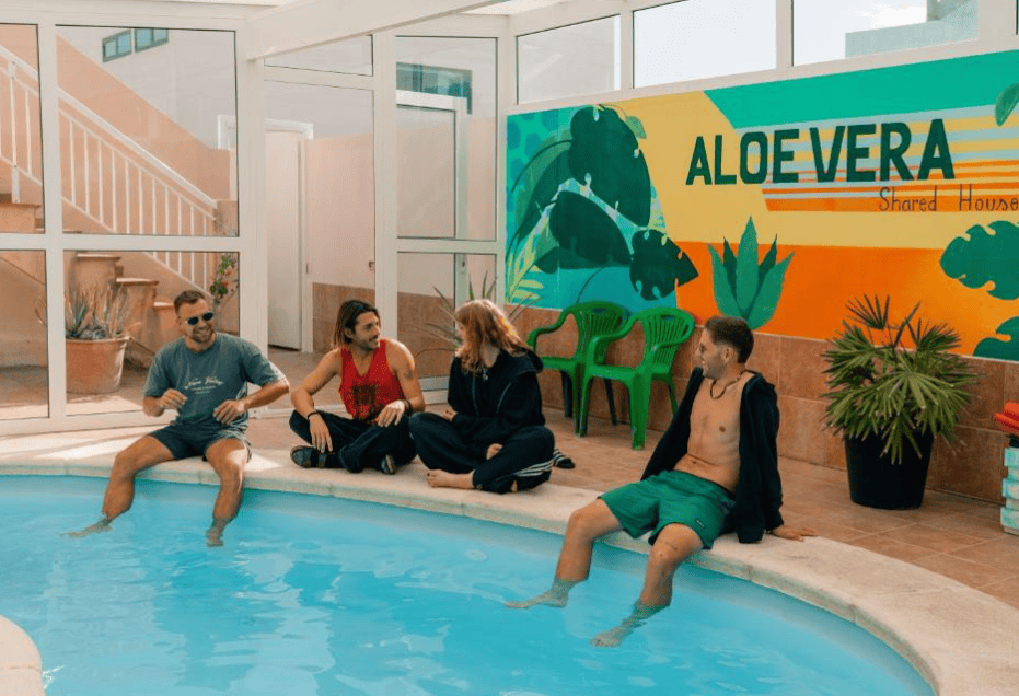 Four young people sitting around a pool at the Aloe Vera shared house near El Médano