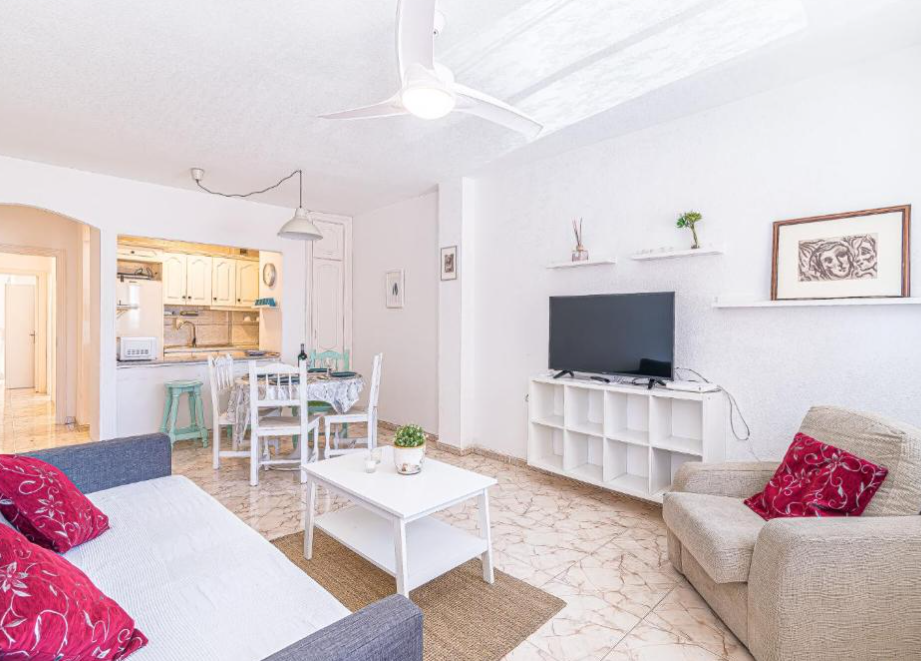 Open space living room with sofa, chair, tv, dining room table. White walls and white fan. 
