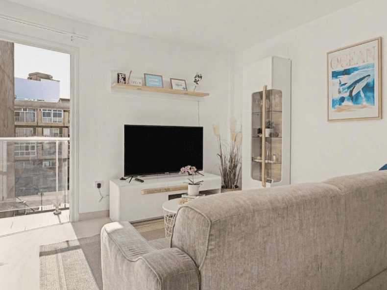 Cheap accommodation in El Médano - a picture of a living room with white walls, grey couch, tv and window looking to the street. 