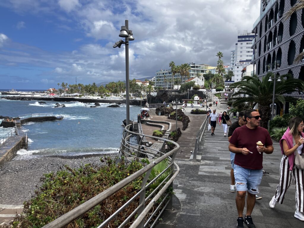 Waterfront promenade in Puerto de la Cruz travel guide. People walking on a street close to Atlantic ocean, palm trees in background
