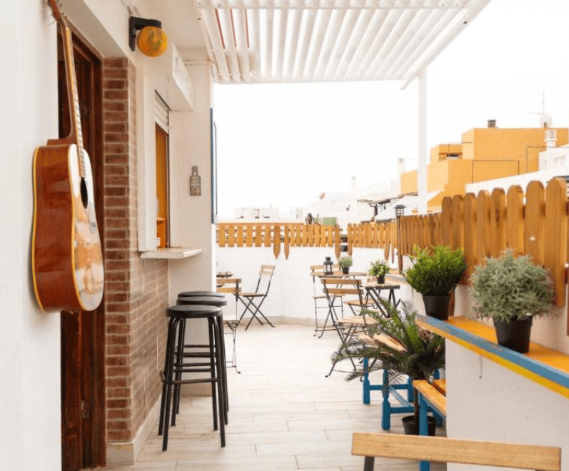 Casa Grande Surf Hostel rooftop terrace with stools, tables and chairs, plants and a guitar hung on the wall